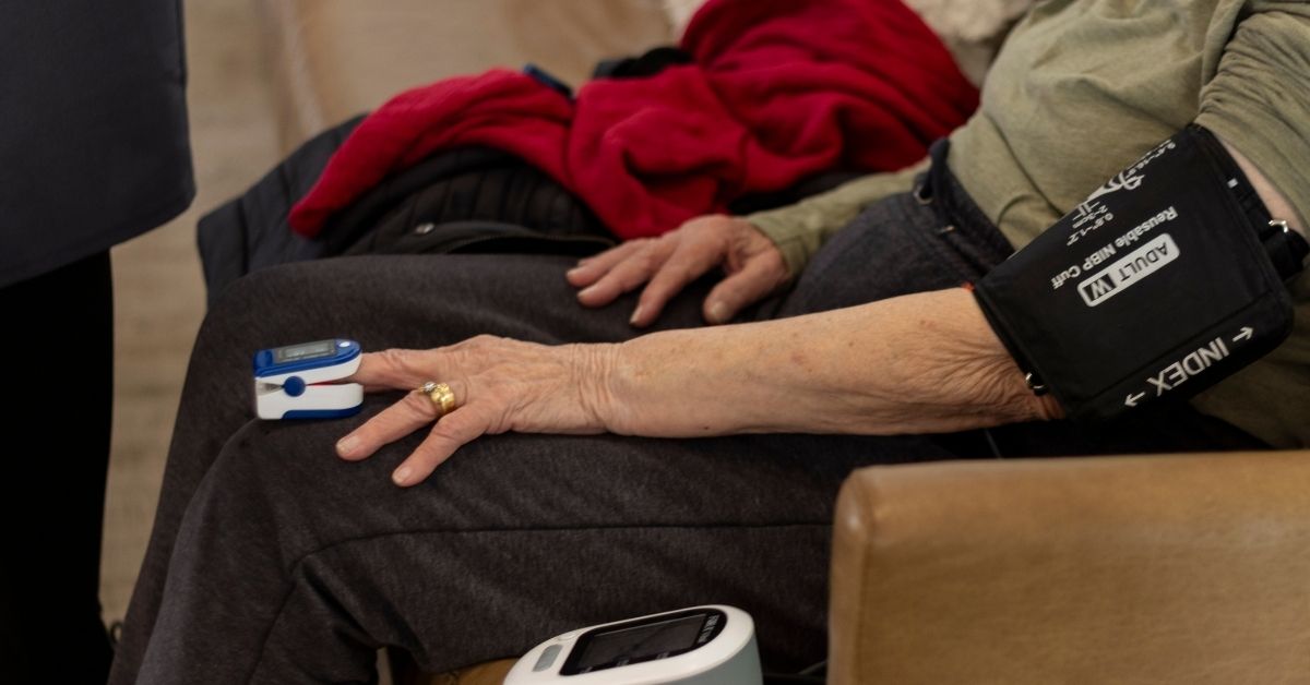 Levels of care in a retirement home where a nurse is checking BP and Sp02 of a residdent sitting on the couch